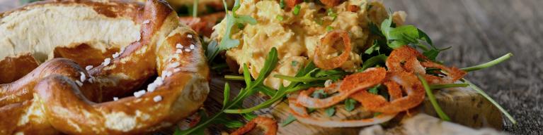 Bayerischer Obazter auf Rucolablättern mit Papikazwiebelringen und Brezel serviert